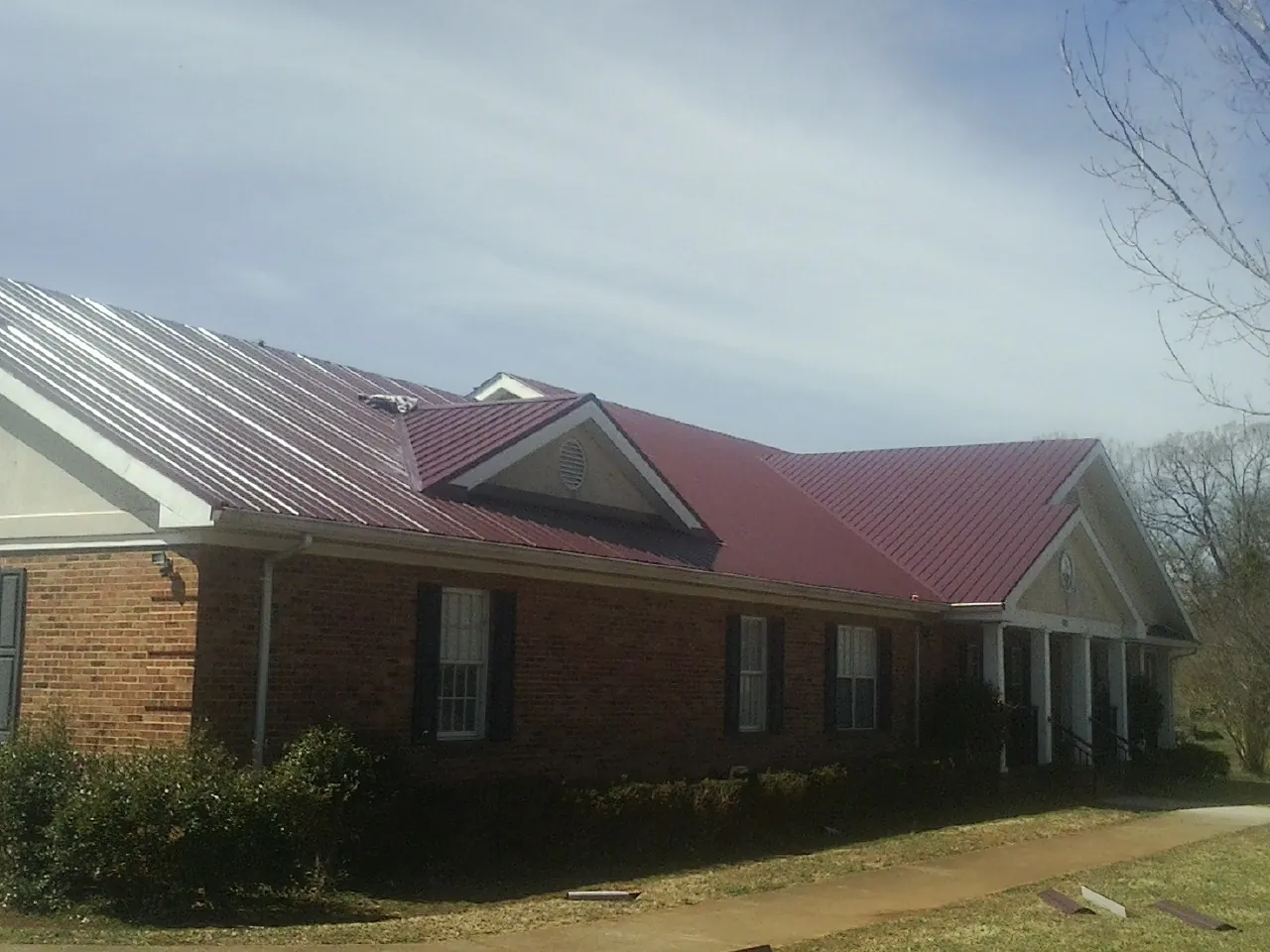 Red metal roof with gabled entries on a long brick building, from a Hail Damage Roof Repair job in Salmon
