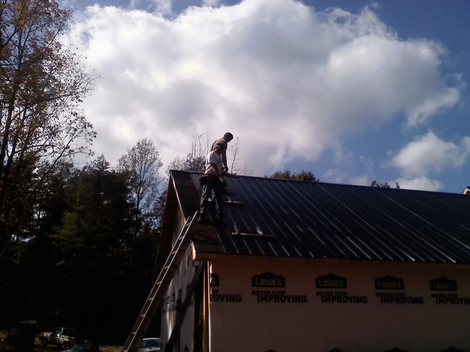 Roofer fastening dark metal panels high against a cloudy sky, from a Roof Inspection job in Salmon